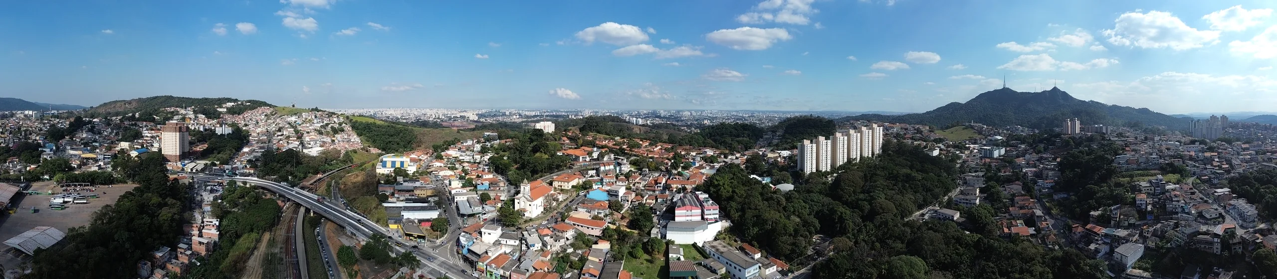 Vista aérea do Jaraguá: viaduto e linha de trem à esquerda, prédios e o Pico do Jaraguá ao fundo, à direita